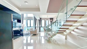 Un interior moderno con una escalera de cristal, una sala de estar con sofá y una mesa de comedor, y una cocina con refrigerador empotrado.