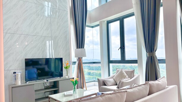 Una sala de estar moderna con una televisión de pantalla plana, un sofá, una mesa de centro y vistas panorámicas de la ciudad a través de amplias ventanas.