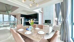Un comedor moderno con una mesa de madera dispuesta para seis personas, rodeada de sillas acolchadas. Un candelabro cuelga encima y hay un florero con flores sobre la mesa.