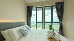Un dormitorio con una cama grande, ropa de cama blanca, un cabecero gris y vistas del paisaje a través de amplios ventanales.