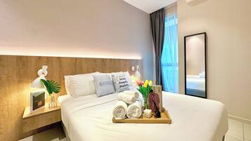 A hotel room with a neatly made bed, a tray with towels and toiletries, a framed picture, and a nightstand with a lamp and a plant.