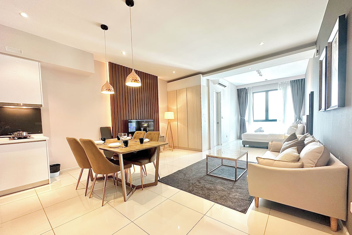 A modern living room with a sofa, a dining area with a table and chairs, a TV, and a kitchen area with a refrigerator.