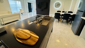 A modern kitchen with a black countertop, wooden cutting boards, and a sink. There is a dining area with black chairs and a white table. - Luxury Hills1500 ㎡ Superb view patio Sauna BBQ 4 parking spaces, swimming pool, pets, near Fukuoka Airport (Kanenokuma, Hakata-ku, Fukuoka City)