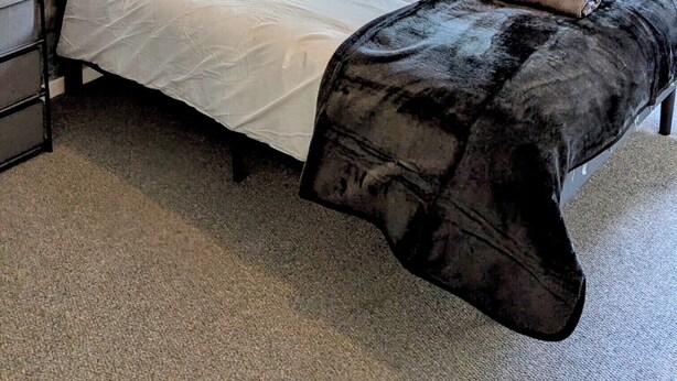 Een slaapkamer met een bed, een nachtkastje, een lamp, een plafondlamp en een raam.