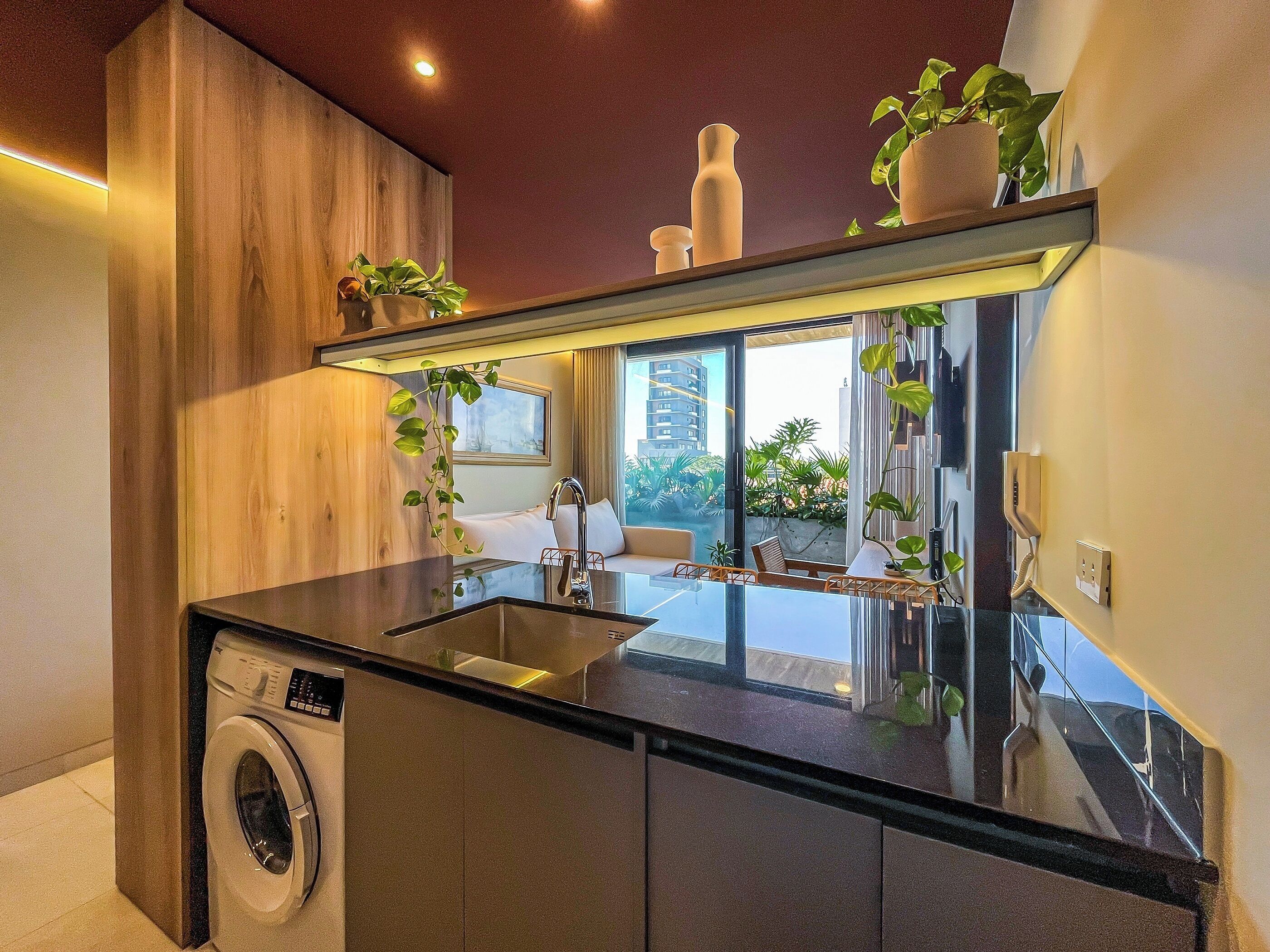 Una cocina moderna con lavadora integrada, un espejo grande y plantas en macetas.