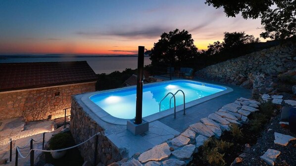 A swimming pool with a stone wall and a view of the sunset.