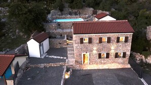 Un edificio de piedra con techo rojo, varias ventanas y una piscina al fondo.