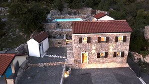 A stone building with a red roof, multiple windows, and a swimming pool in the background.