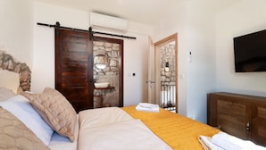 Un dormitorio con cama, armario de madera, televisor montado y pared de piedra.
