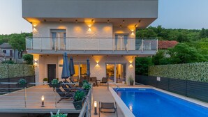 A modern two-story house with a swimming pool, outdoor seating, and a balcony.