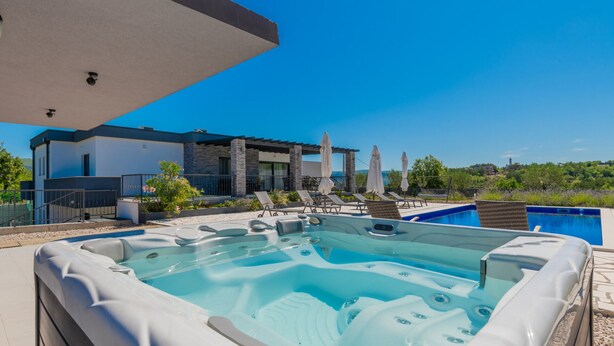 Ein moderner Poolbereich im Freien mit Whirlpool, Liegestühlen und Sonnenschirmen mit Blick auf eine reizvolle Landschaft.