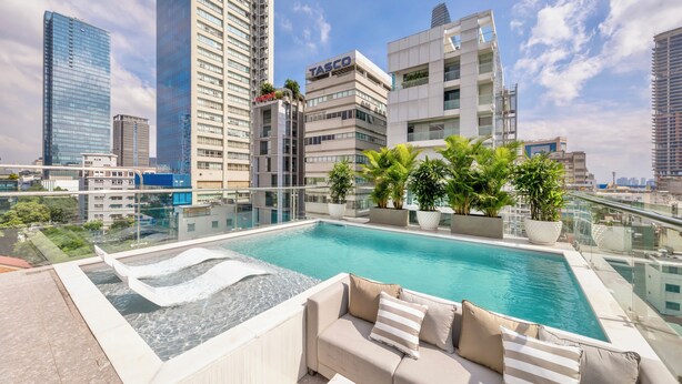 A rooftop pool with a glass barrier, a beige sofa, and potted plants. - IconSphere Hotel (Ho Chi Minh City)