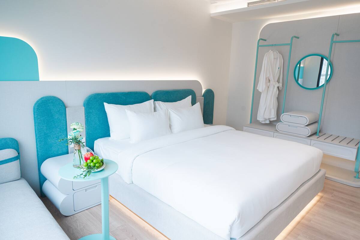 A modern hotel room with a large bed, a bedside table with a vase of flowers, and a bathroom with a robe and towel rack.