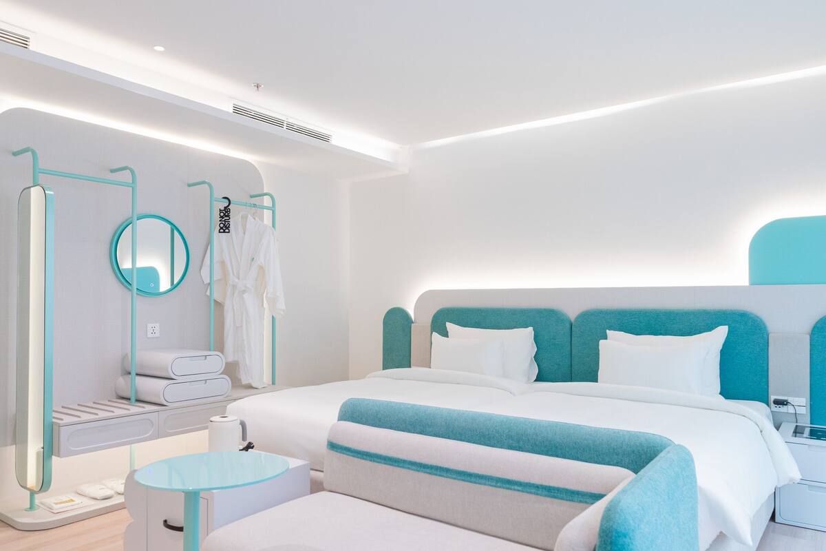 A modern hotel room with a large bed, bedside tables, a round mirror, and a small round table.