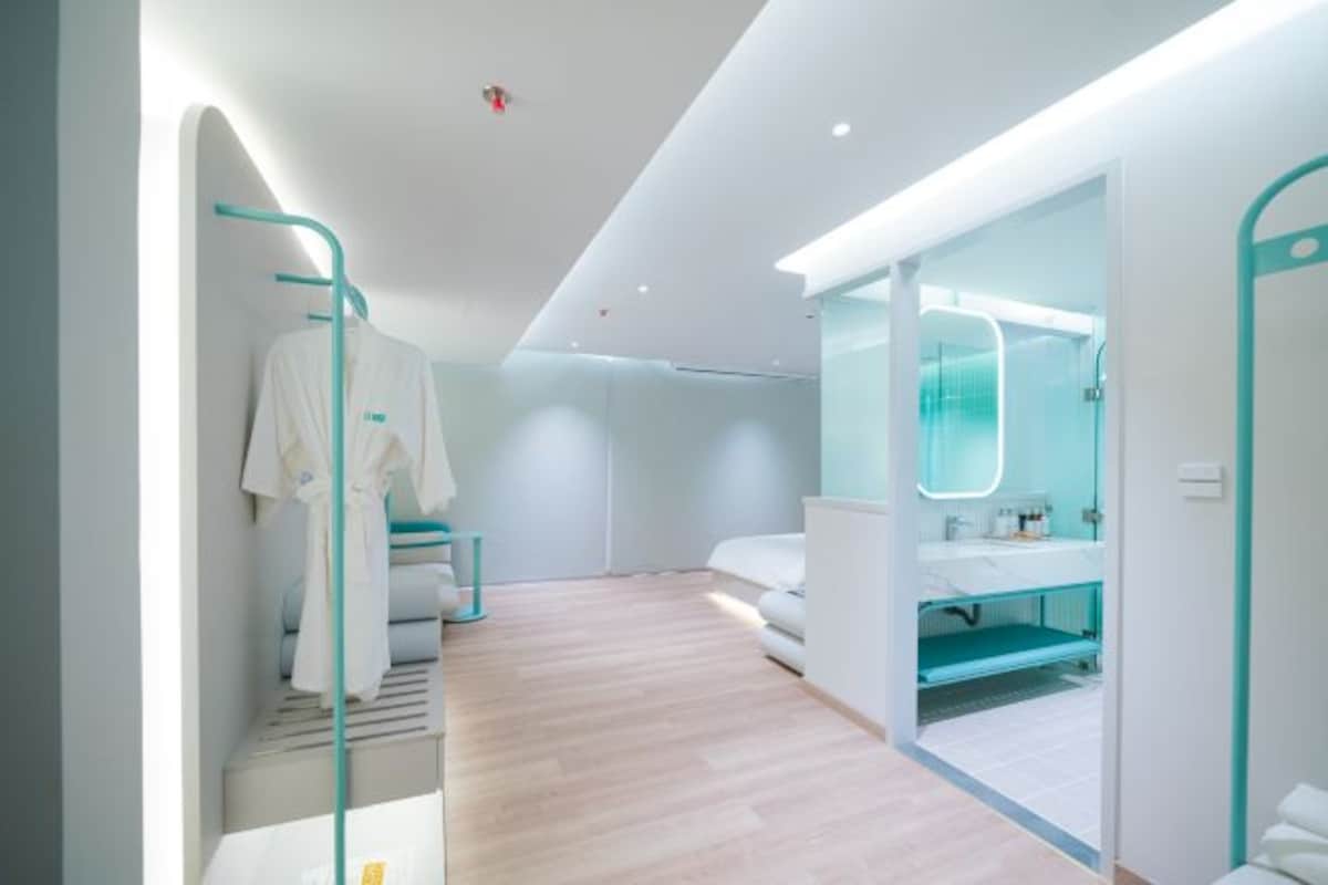 Una habitación de hotel moderna con piso de madera, cabina de ducha de vidrio y baño blanco con cabina de ducha de vidrio.