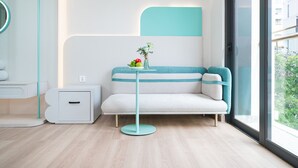 A modern, minimalist room with a white sofa, a small round table with a vase of flowers, and a large window offering a view of buildings and greenery. - IconSphere Hotel (Ho Chi Minh City)