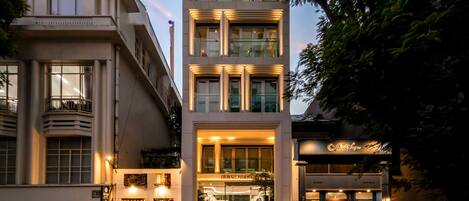 Un edificio de varios pisos con un diseño arquitectónico moderno, que destaca por una entrada imponente y una escalera visible que conduce a la planta baja.