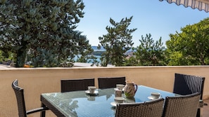 Ein Tisch mit Stühlen und einer Kanne, vor einer Baumlandschaft und Blick auf das Meer.
