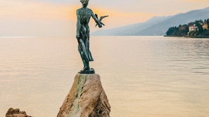 A statue on a rock by a calm body of water with mountains in the background.