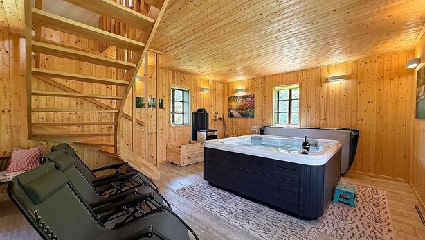 A wooden cabin interior with a hot tub, a staircase, and a massage chair.