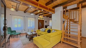 A living room with a yellow sofa, a wooden staircase, and a green chair.