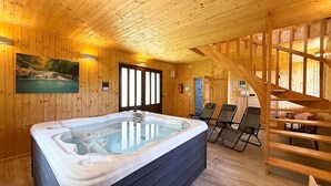 A wooden cabin interior with a hot tub, wooden walls, a painting, and a staircase.
