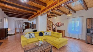 A living room with a yellow sofa, wooden beams, a staircase, and a dining area.