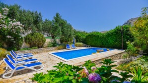 A pool area with blue lounge chairs, a swimming pool, and surrounding greenery.