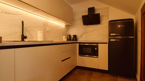 Una cocina compacta con un refrigerador negro, un horno Bosch y una salpicadera de mármol.
