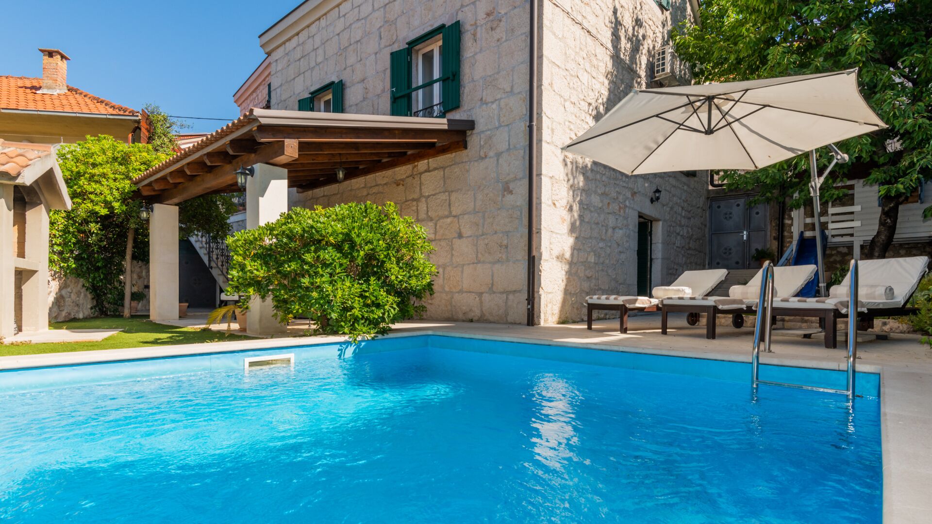 A swimming pool with a pergola and lounge chairs, surrounded by stone buildings.