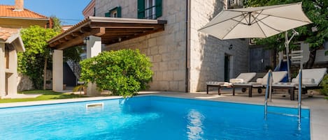 A swimming pool with a pergola and lounge chairs, surrounded by stone buildings.