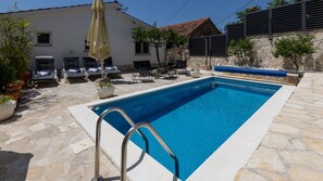 Una piscina rectangular con una escalera metálica, rodeada de baldosas de piedra y plantas en macetas.