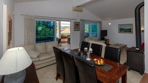 A spacious living area with a sofa, dining table, and chairs. There is a large window providing a view of the outdoors.