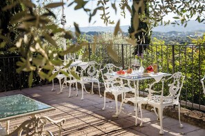 Un patio exterior con sillas y mesas de metal blanco, una mesa de vidrio y vistas al campo.