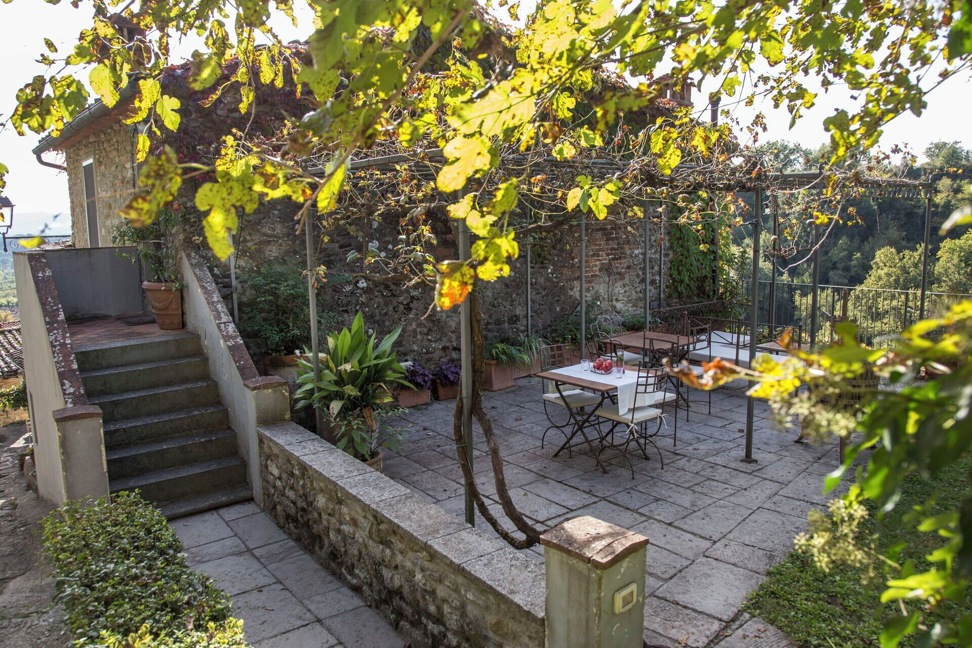 Une terrasse avec une table et des chaises, entourée de plantes et d’un mur en pierre.