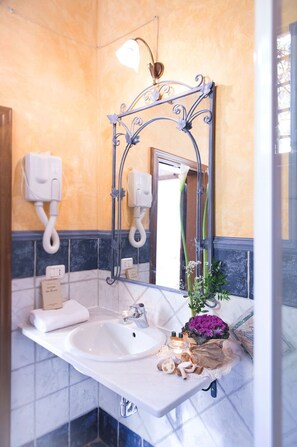 Un baño con un lavamanos blanco, un espejo con marco decorativo, un perchero y un dispensador de jabón para manos.