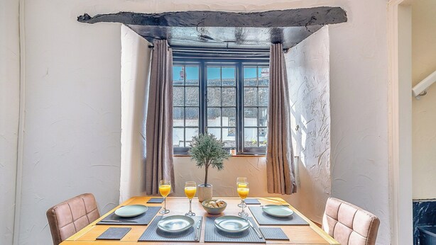 A dining area with a table set for four, a small potted plant, and a window with curtains. - 2 bedroom accommodation in Umberleigh (Umberleigh)