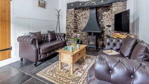 A cozy living room with a stone wall, a fireplace, a television, and leather sofas. - 2 bedroom accommodation in Umberleigh (Umberleigh)