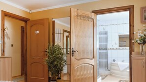 A hotel room with a wooden door, a potted plant, a bed with a pink blanket, and a view of the bathroom through an open door. - 5 bedroom accommodation in Gamston, near Nottingham (Gamston, near Nottingham)