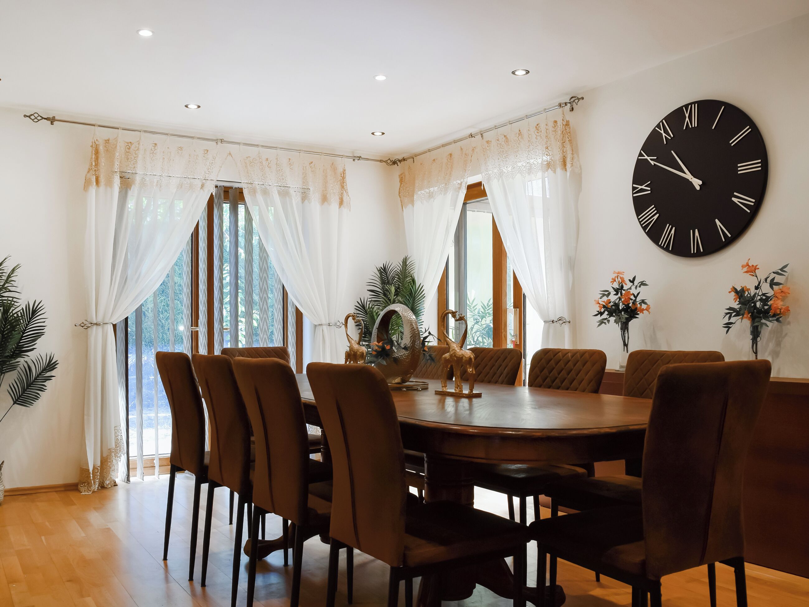 A dining room with a round table, brown chairs, and a large wall clock.