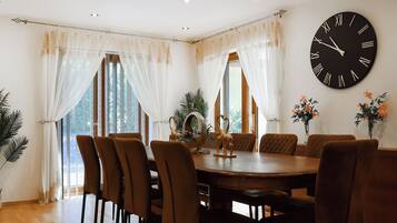 A dining room with a round table, brown chairs, and a large wall clock.