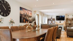 A modern living room with a dining area, featuring a large clock, a cityscape painting, and a fireplace. - 5 bedroom accommodation in Gamston, near Nottingham (Gamston, near Nottingham)