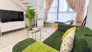 A modern living room with a green sofa, a flat-screen TV, a staircase, and a large window with curtains. - Kuchai Sentral by Manhattan Group (Kuala Lumpur)
