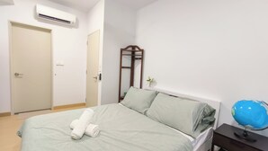 A neatly made bed with a rolled towel, a wooden nightstand with a globe, and a wall-mounted air conditioner. - Kuchai Sentral by Manhattan Group (Kuala Lumpur)