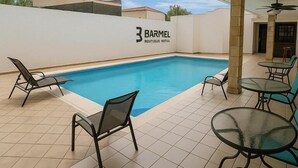 Un espace piscine avec des chaises longues et une table, un ventilateur de plafond, et un bâtiment sur lequel on peut lire l’inscription « 3 BARMEL ».