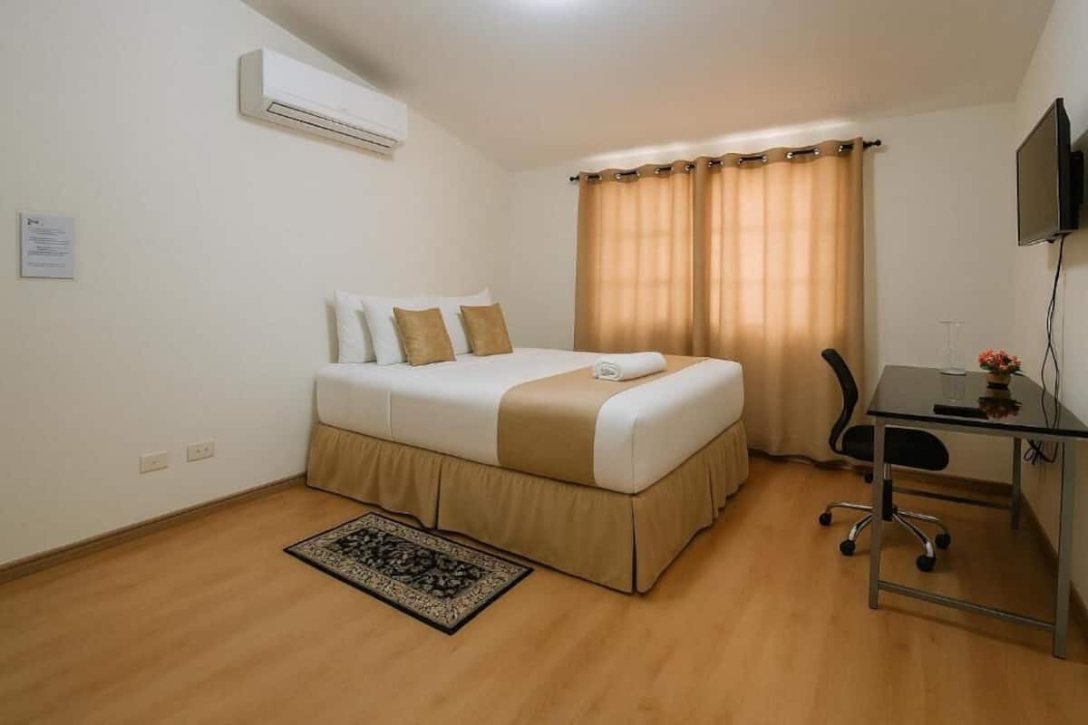Een hotelkamer met een bed, een bureau, een stoel, een airconditioner en een televisie.