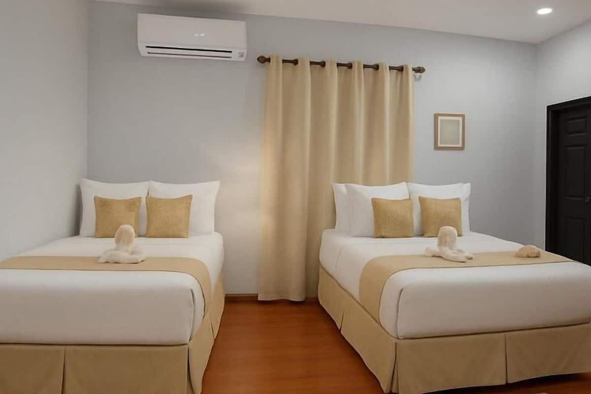 Een hotelkamer met twee bedden, beige beddengoed, een houten vloer, een airconditioning en een zwarte deur.