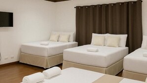 Une chambre d’hôtel avec deux lits simples et un lit double, tous dotés de draps et d’oreillers blancs.