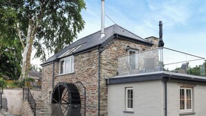 Una casa de piedra con una noria grande, un balcón con mobiliario exterior y un pequeño jardín.