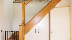 Una escalera de madera con un muro de piedra arriba, que conduce a un cuarto con armarios blancos y barandilla de metal negro.